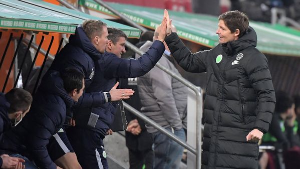 VfL-Wolfsburg-Trainer Oliver Glasner klatscht sich mit seinen Co-Trainern ab und jubelt. 