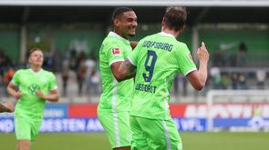 Die VfL-Wolfsburg-Spieler Maxence Lacroix und Wout Weghorst lachen sich an und freuen sich über das erzielte Tor. 