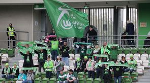 Die Fans der Frauenmannschaft des VfL wolfsburg sitzen auf der Tribüne, halten ihre Schals in die Höhe und schwenken eine Fahne.