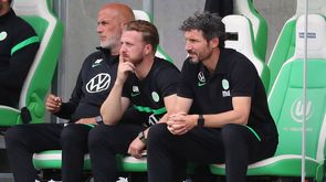 Das Trainerteam des VfL Wolfsburg sitzt auf der Trainerbank.